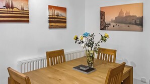 Une salle à manger avec une table en bois, quatre chaises, un vase de fleurs et trois tableaux accrochés au mur.