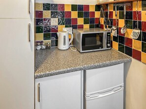 A kitchen with a microwave, kettle, and various utensils.