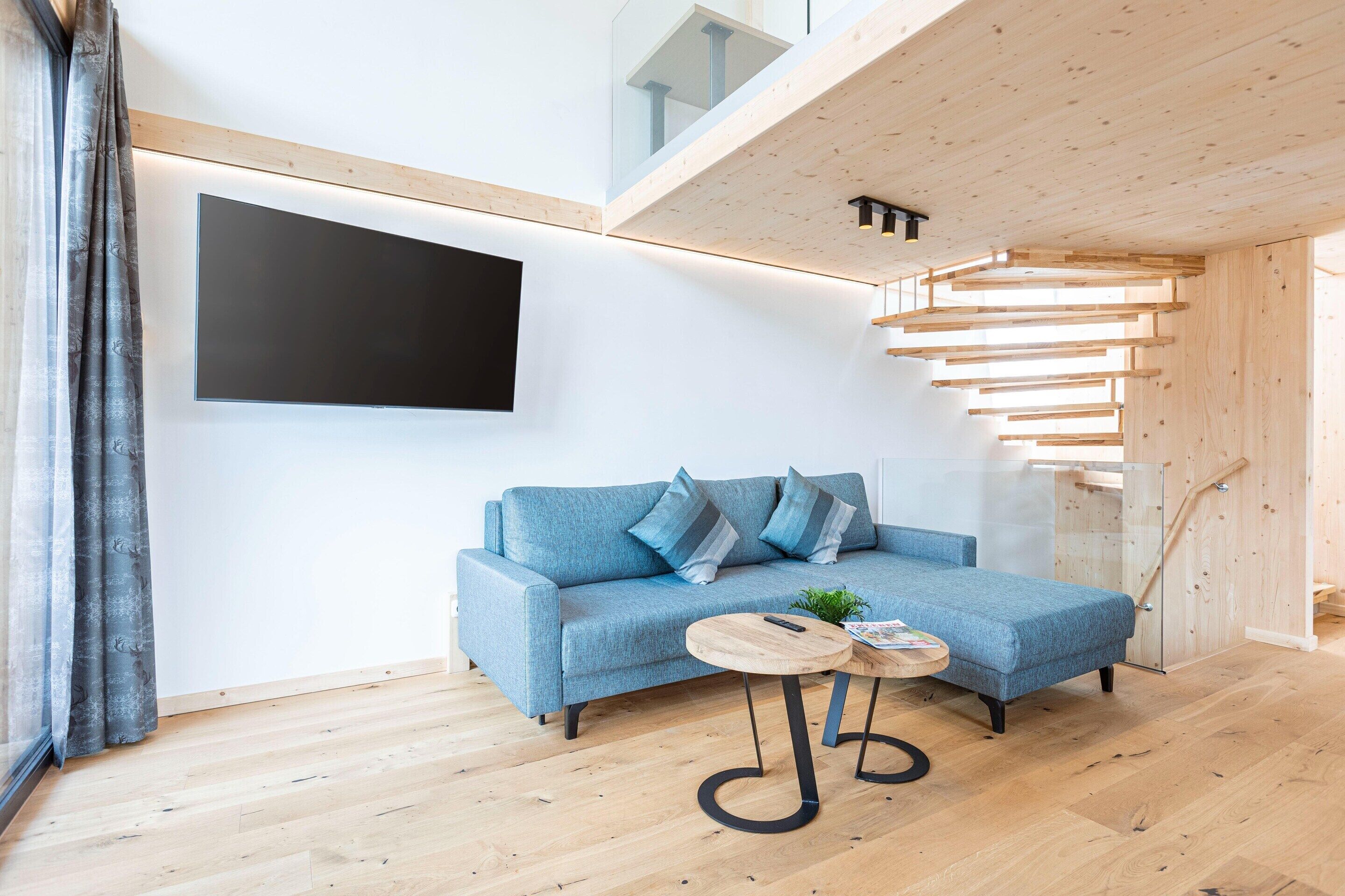 A modern living room with a blue sofa, a small round table, and a staircase with wooden railings.