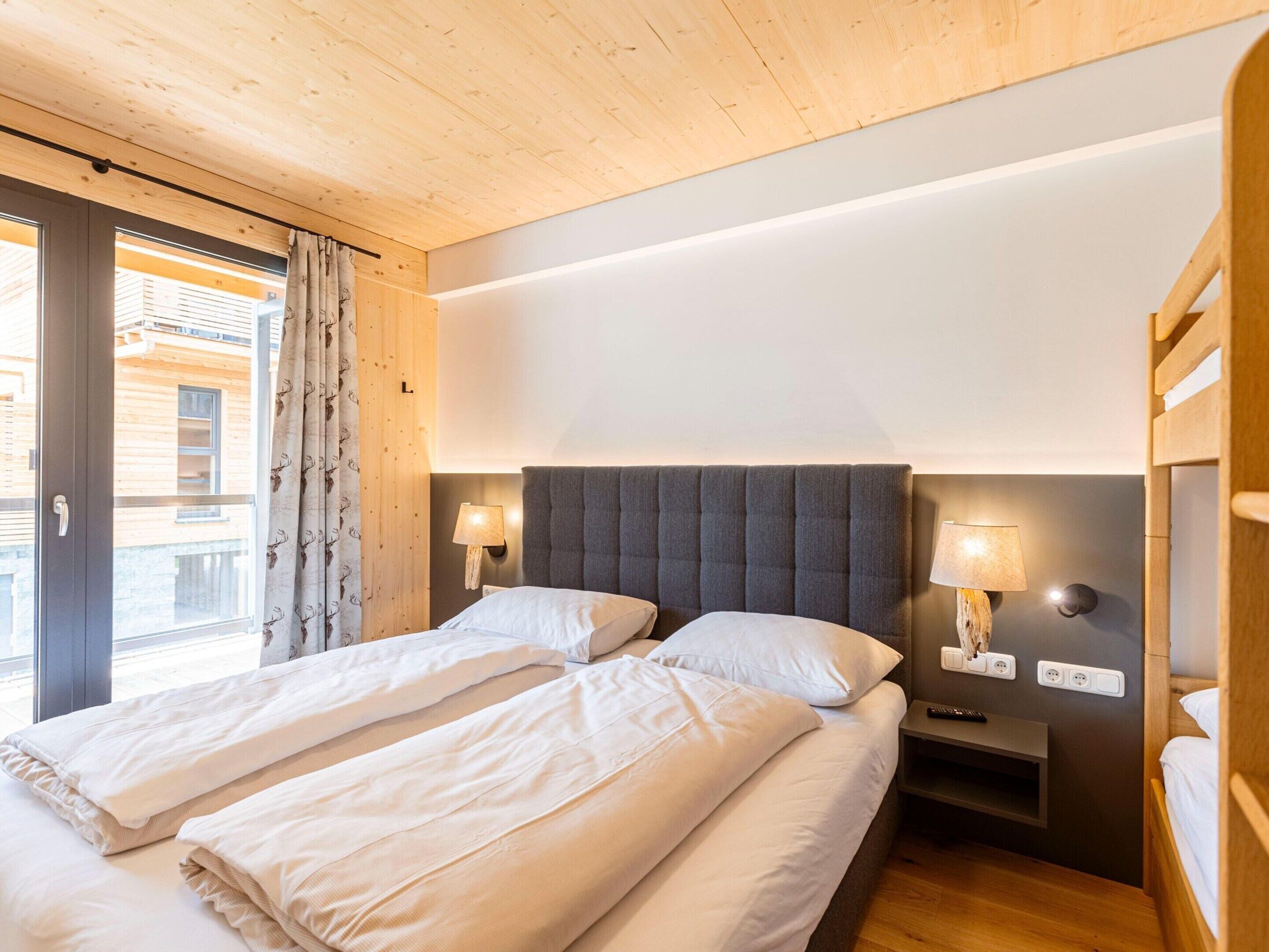 A double bed with two pillows, a bedside table with a lamp, and a window with curtains.