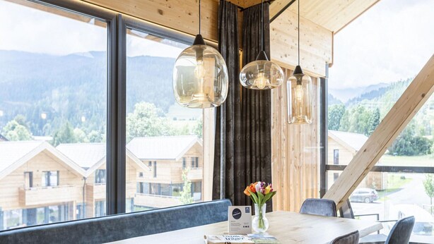 A modern dining area with a wooden table and chairs, large windows offering a view of the surrounding buildings and mountains. - Stylish Penthouse With Sauna (Sankt Georgen am Kreischberg)