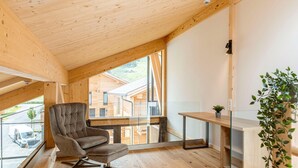 A modern wooden interior with a high ceiling, a cushioned chair, a small table, and a view of neighboring buildings. - Stylish Penthouse With Sauna (Sankt Georgen am Kreischberg)