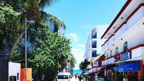 A street with shops, a white van, and people walking. - Room with balcony at BLVD Hotel, fifth avenue (Playa del Carmen)
