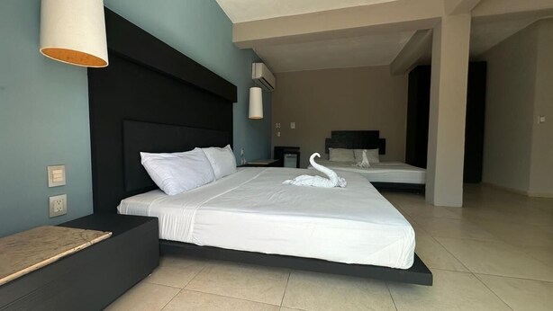 A modern hotel room with a large bed, a bedside table, a wall-mounted lamp, and a view of the hallway. - Room with balcony at BLVD Hotel, fifth avenue (Playa del Carmen)