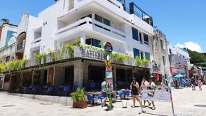 A white building with a restaurant named "EATITAI" on the ground floor, outdoor seating, and a signboard. - Room with balcony at BLVD Hotel, fifth avenue (Playa del Carmen)