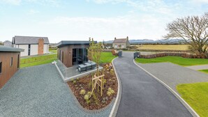 Un edificio moderno con un patio, un muro de piedra y un campo cubierto de césped al fondo.