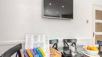 A dining area with a glass table, black chairs, a TV mounted on the wall, and a menu on the table.