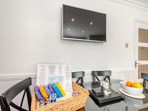 A dining area with a glass table, black chairs, a TV mounted on the wall, and a menu on the table.