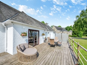 Una terraza de madera con mobiliario exterior, una silla de mimbre y una mesa.