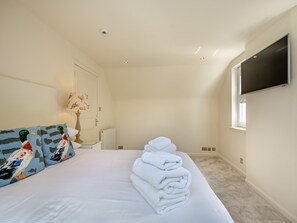 Un dormitorio con cama, almohadas, televisor, radiador y ventana.