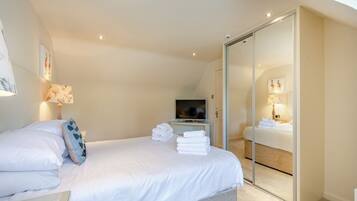 A modern hotel room with a bed, a TV, a glass door closet, and a wall-mounted lamp.