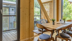 A wooden interior with a dining table, chairs, and a view of a balcony with a railing.