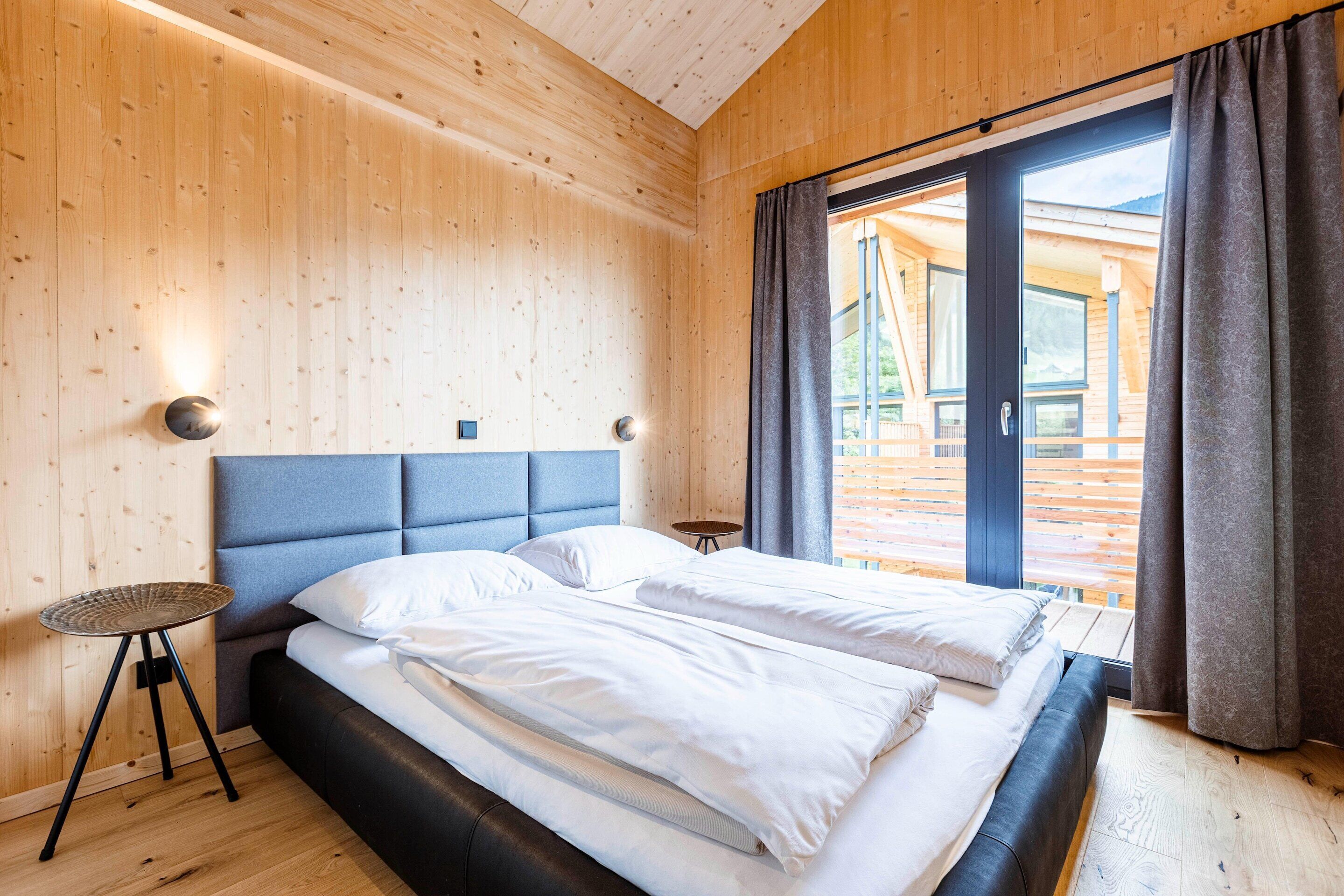 Une chambre moderne avec un grand lit, des murs en bois et une vue sur l’extérieur.