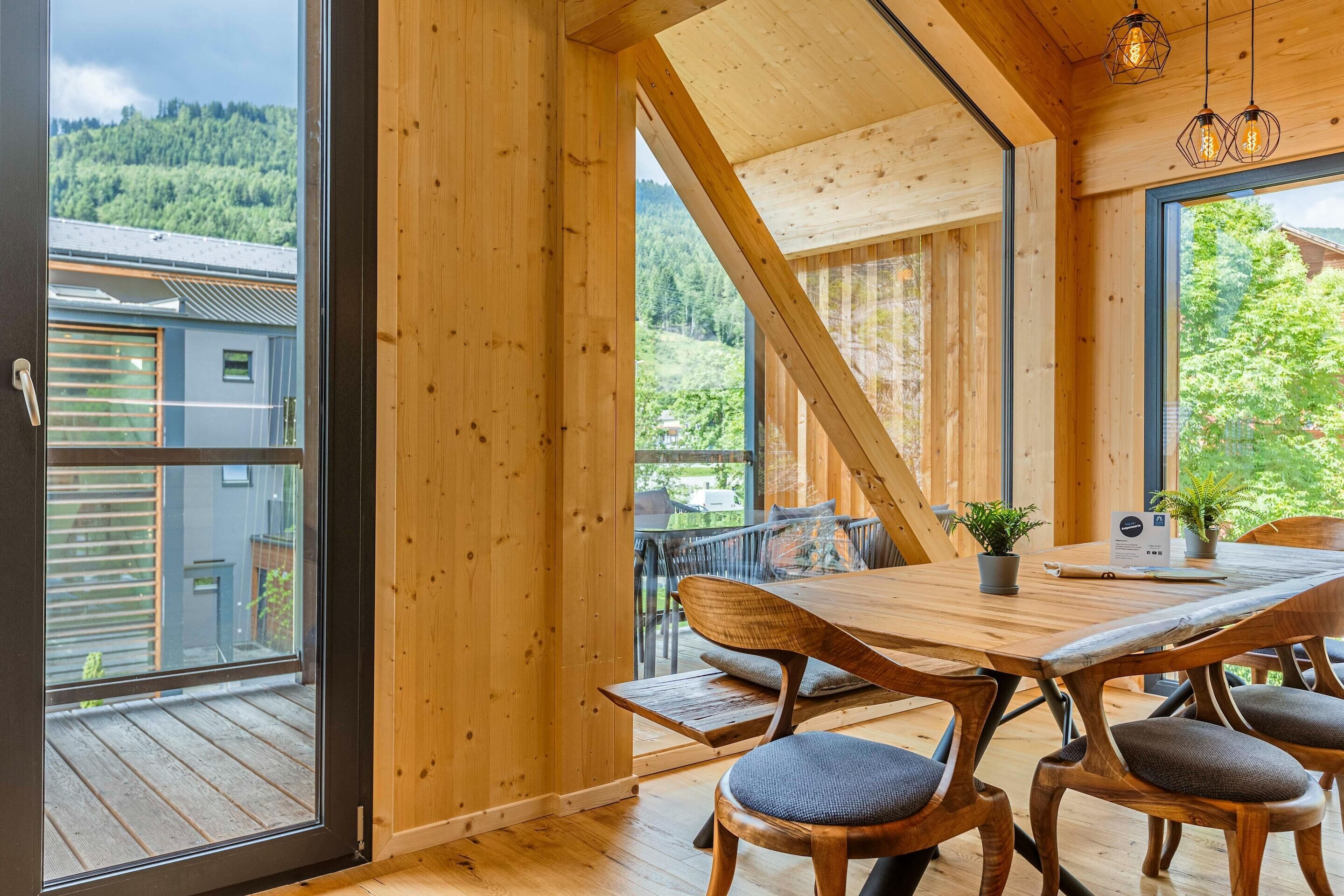 Un intérieur en bois avec une table et des chaises, de grandes fenêtres et une vue sur une zone boisée.