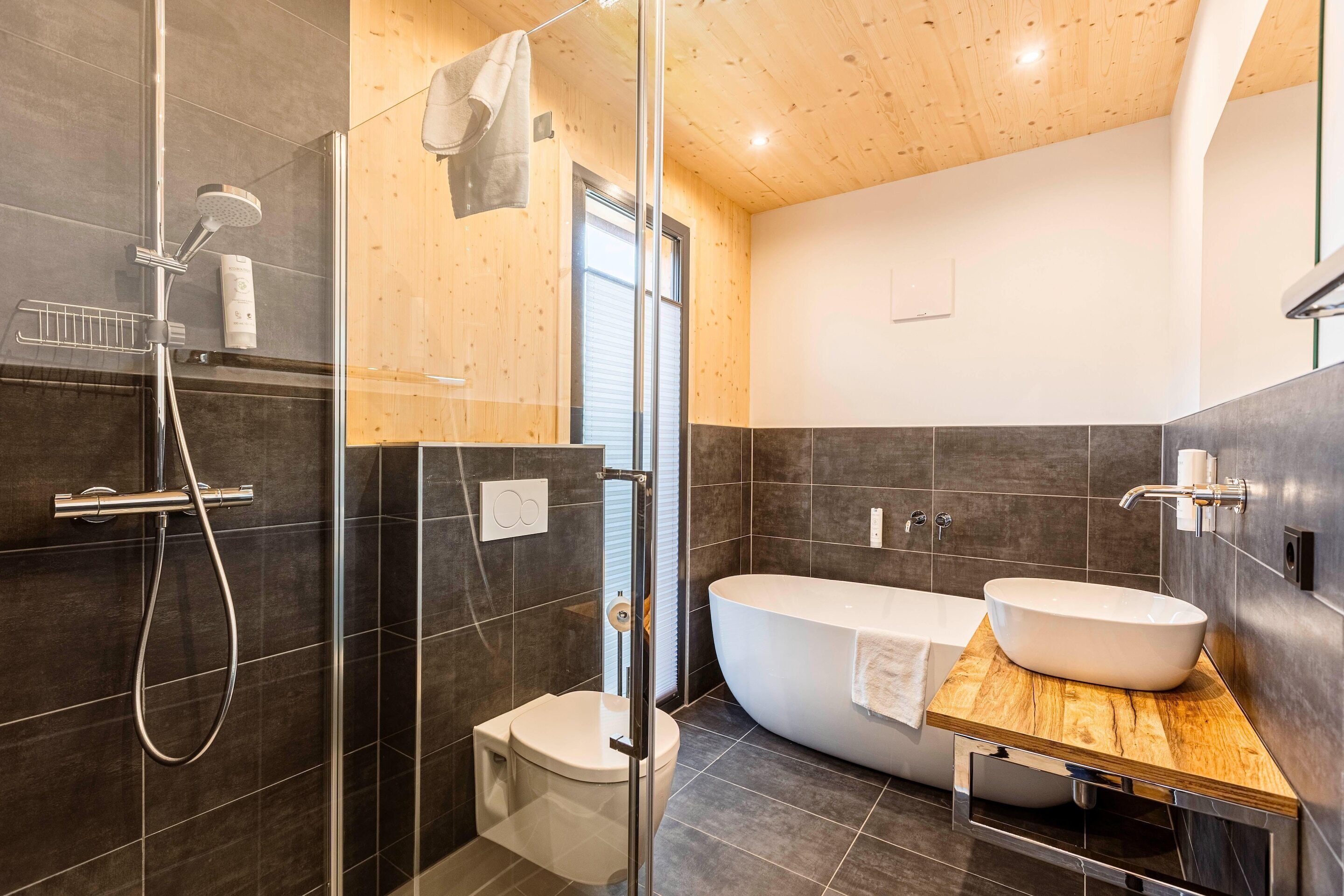 Une salle de bain moderne dotée d’une douche à parois de verre, de toilettes sur pied et d’une baignoire îlot avec un meuble-lavabo en bois.