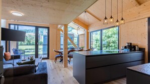 A modern kitchen with a large island, wooden ceiling, and large windows offering a view of the outdoors.