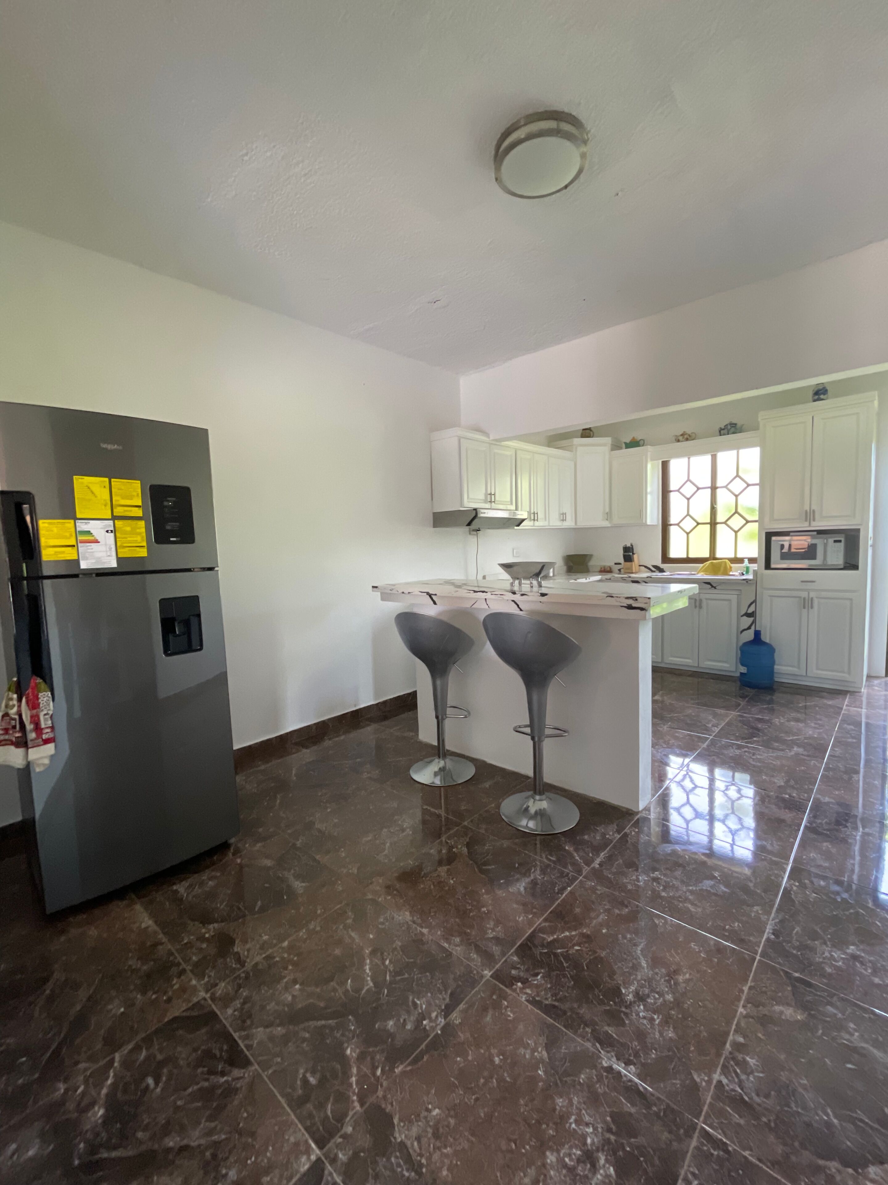 A modern kitchen with a refrigerator, bar stools, and white cabinets.
