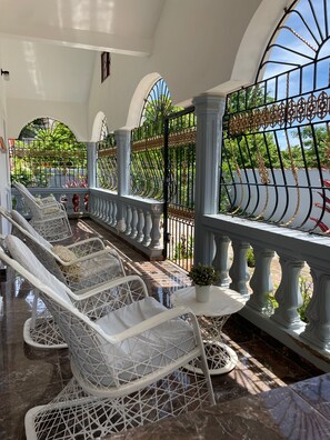 A covered outdoor seating area with white wicker chairs and a metal railing.