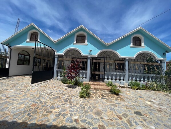 A two-story house with a stone-paved courtyard, decorative metal gates, and a blue facade.