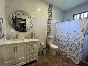 A bathroom with a marble floor, a toilet, a sink with a mirror, and a shower curtain.