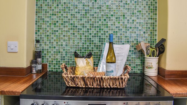 A kitchen with a green mosaic backsplash, a basket of bread, a bottle of wine, and kitchen utensils. - 2 bedroom accommodation in Hovingham, near Helmsley (Hovingham, near Helmsley)