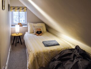 Une petite chambre à coucher, chaleureuse et accueillante, avec un lit simple, une lampe de chevet, un ours en peluche et une fenêtre donnant sur les arbres.