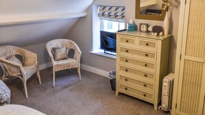 A room with two wicker chairs, a dresser, a radiator, and a window with curtains. - 2 bedroom accommodation in Hovingham, near Helmsley (Hovingham, near Helmsley)
