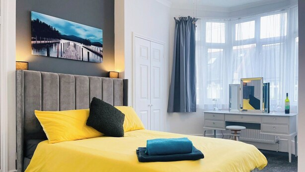 Habitación de hotel con cama, escritorio, silla, espejo y ventana con cortinas.