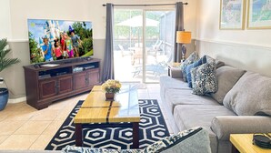 A living room with a flat-screen TV, a sofa, a coffee table, and a view of the outdoors through a sliding glass door. - 4 Bedroom villa - private pool & game room near Disney (Kissimmee)