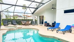 An indoor swimming pool with lounge chairs and a table, surrounded by a glass enclosure with a view of palm trees and houses. - 4 Bedroom villa - private pool & game room near Disney (Kissimmee)