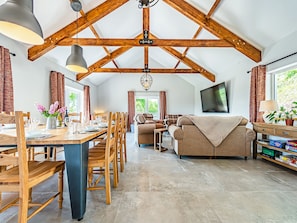 A spacious room with a high ceiling, wooden beams, a dining area with a table and chairs, a sofa, a television, and a bookshelf. - 5 bedroom accommodation in Llansawel, near Llandeilo (Llansawel, near Llandeilo)