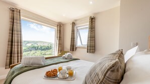 A hotel room with a large bed, a breakfast tray with croissants and juice, and a view of green hills. - 5 bedroom accommodation in Llansawel, near Llandeilo (Llansawel, near Llandeilo)