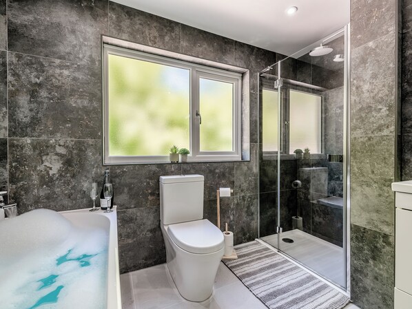 A modern bathroom with a bathtub, toilet, and glass-enclosed shower.