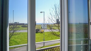 A view from a window with a metal fence, a road, and a building in the distance.