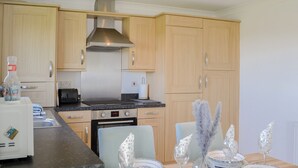 A modern kitchen with wooden cabinets, a stainless steel range hood, and a dining area set with plates, glasses, and cutlery.