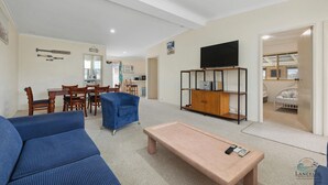 A living room with a sofa, a coffee table, a TV on a stand, and a dining area with chairs and a table. - Aqua Sands Chalets-Nestled in the heart of Lancelin (Lancelin)