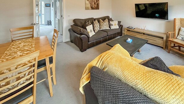 A living room with a sofa, a coffee table, a TV, and a dining area with chairs and a table. - 3 bedroom accommodation in Inverness (Inverness)