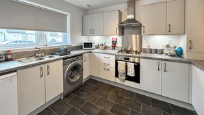 A modern kitchen with a washing machine, oven, microwave, and stainless steel range hood. - 3 bedroom accommodation in Inverness (Inverness)