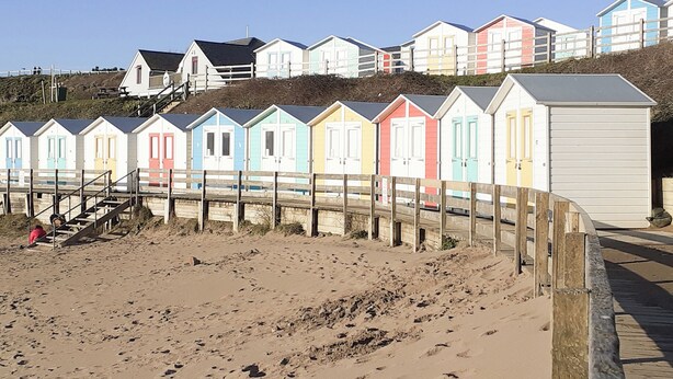 A row of colorful beach huts with a sandy beach and wooden boardwalk in the foreground. - 2 bedroom accommodation in Bude (Bude)
