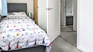 A bedroom with a bed, a nightstand, a lamp, and a door leading to a bathroom. - 2 bedroom accommodation in Bude (Bude)