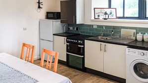 A compact kitchen with a microwave, dishwasher, and washing machine. There is a dining table with chairs and a window above the sink. - The Old Mill Apartment - UK48028 (Tain)