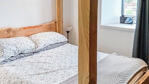 A bedroom with a wooden headboard, a bed with patterned bedding, a bedside lamp, and a window with a view of the outside. - The Old Mill Apartment - UK48028 (Tain)
