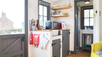 Une cuisine compacte équipée d’un four à micro-ondes, d’un grille-pain et d’un bloc à couteaux sur le plan de travail. Des couvertures anti-feu et des maniques sont accrochées au mur.