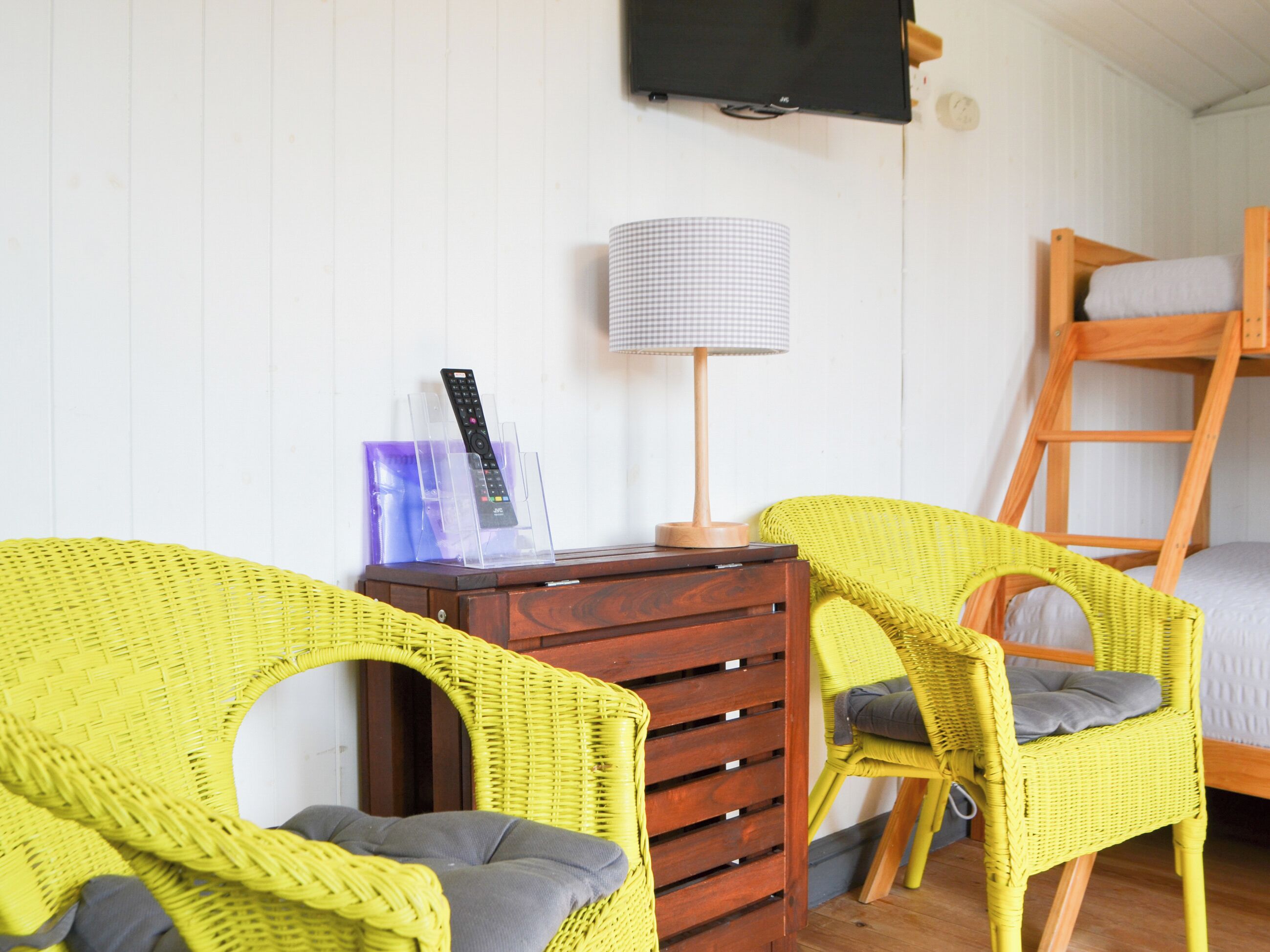 Une pièce comprenant deux fauteuils en osier jaune, une commode en bois, une lampe, un téléviseur et un lit superposé.