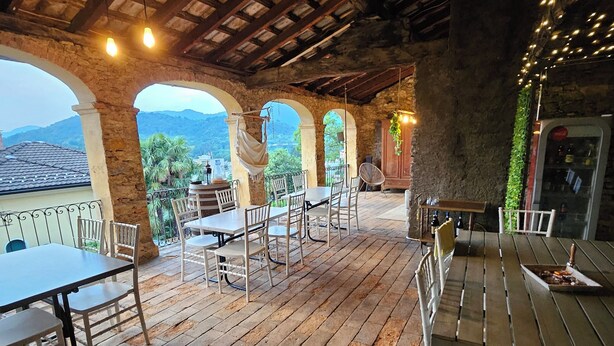 An outdoor patio with rustic stone walls, wooden beams, and tables and chairs. - Francy (Ponte Capriasca)