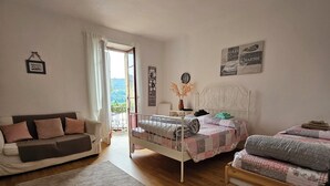 A bedroom with two beds, a sofa, a wooden floor, and a view of the outdoors. - Francy (Ponte Capriasca)