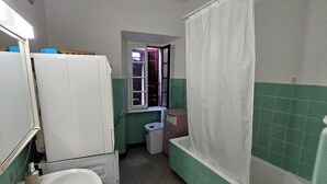 A bathroom with a sink, mirror, bathtub, and a window with a curtain. - Francy (Ponte Capriasca)