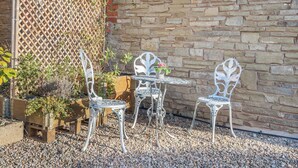 En terrasse med to metalstole og et lille bord, omgivet af grus og krukker med planter.