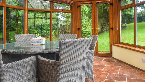 A conservatory with a glass table and wicker chairs, surrounded by large windows and a view of a garden. - 4 bedroom accommodation in Hainworth, near Keighley (Hainworth, near Keighley)