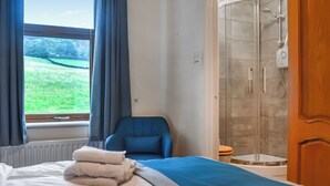A hotel room with a bed, a chair, a shower, and a view of a green field through the window. - 4 bedroom accommodation in Hainworth, near Keighley (Hainworth, near Keighley)